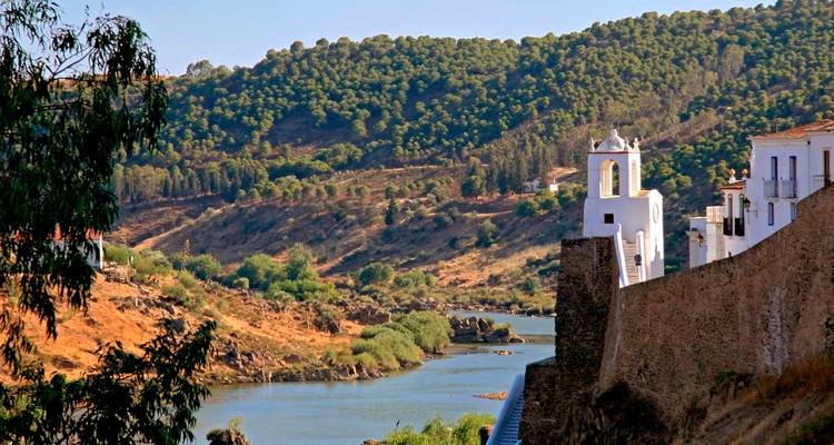 Quiet riverside scene of whitewashed hilltop village and church tower overlooking Guadiana River