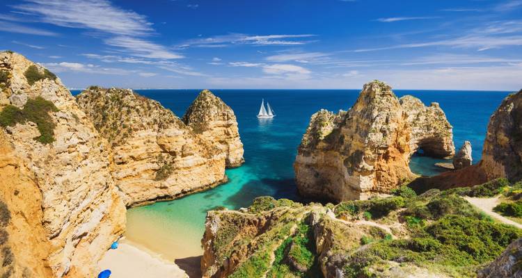 Dramatic limestone rock formations and a sailing boat on crystal blue water at Ponta da Piedade near Lagos.