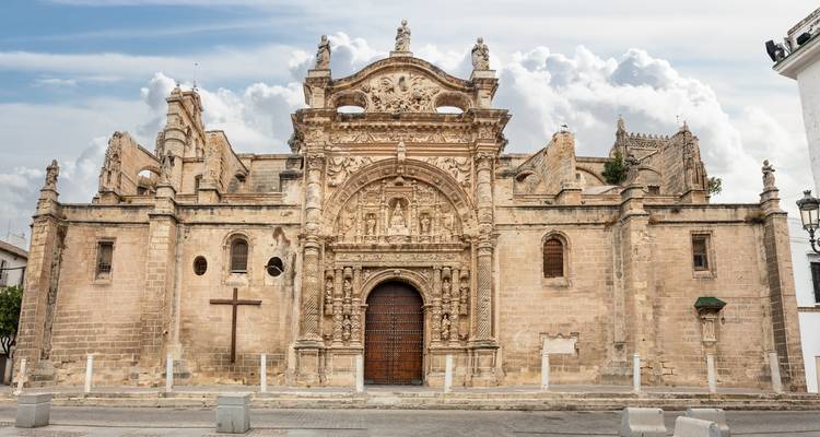 Façade d'église en pierre historique avec des sculptures ornées et une lourde porte en bois sous des nuages doux.