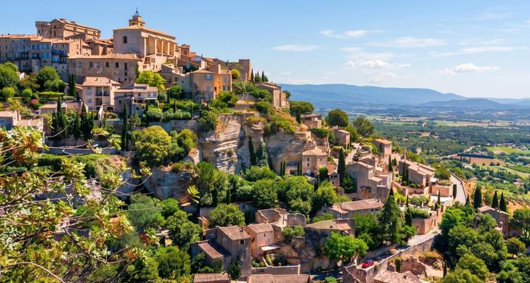 Village perché de Gordes dominant une vallée provençale luxuriante sous un ciel ensoleillé.