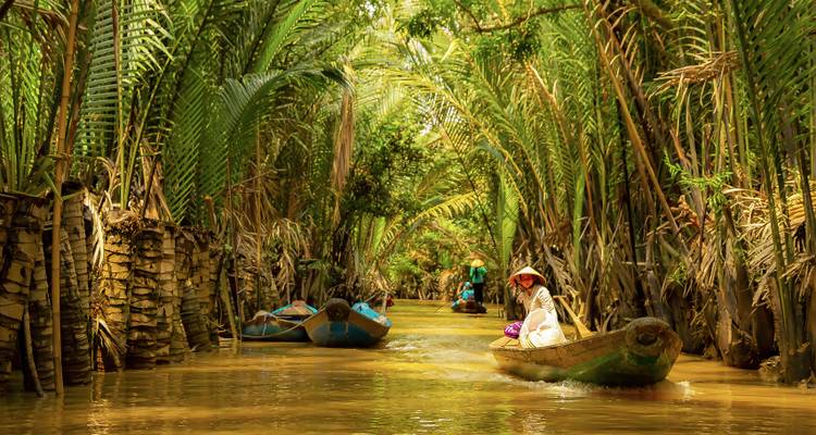 Traditional sampans glide through narrow golden waterways framed by towering palms.