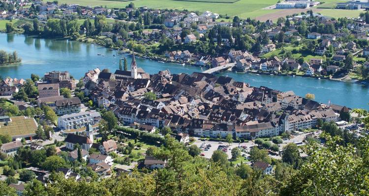 Vue panoramique élevée d'une ville médiévale compacte sur un méandre de rivière, entourée par une campagne verdoyante en Suisse.