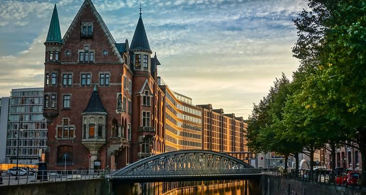 La lumière du soir frappe les entrepôts en briques rouges et un petit pont enjambant un canal tranquille dans le Speicherstadt de Hambourg.