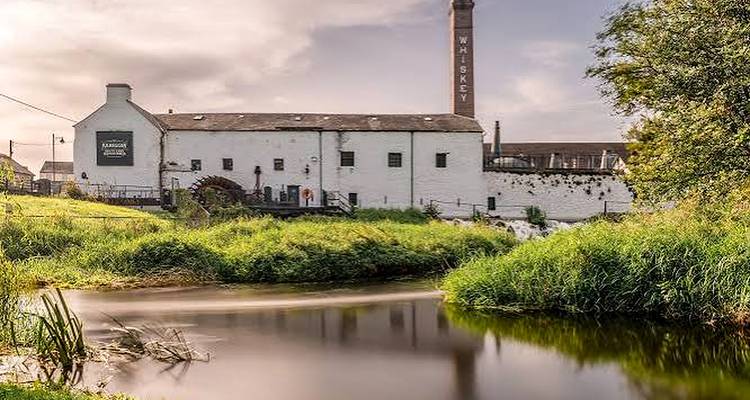 L'entrepôt de la distillerie de whiskey historique de Kilbeggan et sa haute cheminée située à côté d'une rivière à courant lent.