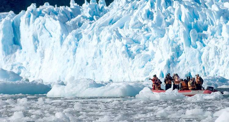 Travelers in a rubber dinghy explore icy waters filled with small chunks of ice near a glacier.