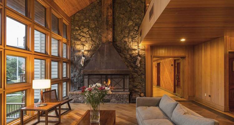 Un acogedor salón con chimenea de piedra e interiores de madera, iluminado suavemente para relajarse por la noche.