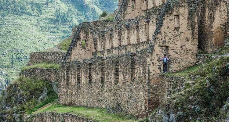 Voyageur se tenant parmi les magasins de pierre d'Ollantaytambo se dressant face aux falaises andines verdoyantes