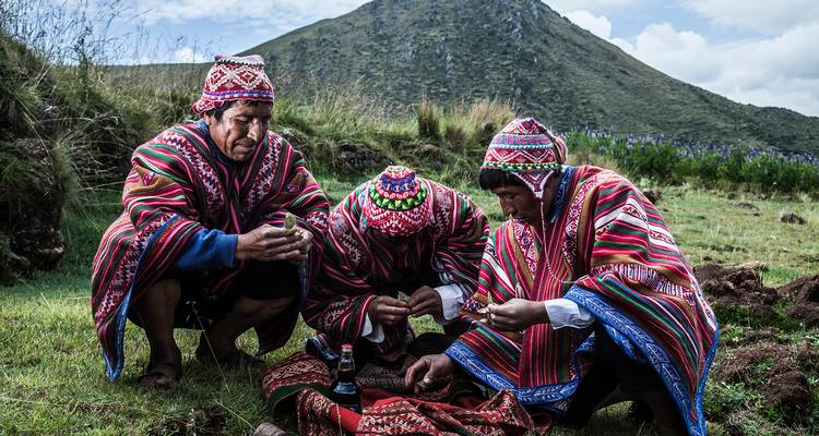 Trois hommes quechuas vêtus de ponchos traditionnels aux couleurs éclatantes effectuant un rituel dans une prairie de montagne