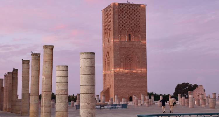 La Torre Hassan brilla suavemente en color rosa al atardecer entre columnas en ruinas.