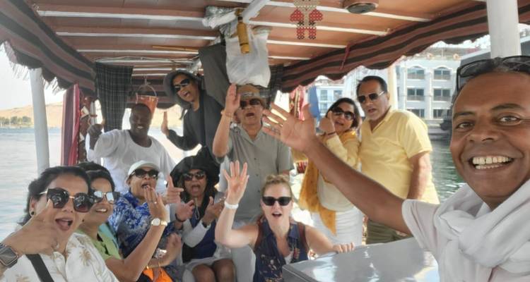 Un groupe de touristes enthousiaste fait des signes d'adieu depuis un petit bateau à moteur sur le Nil avec des hôtels riverains en arrière-plan.