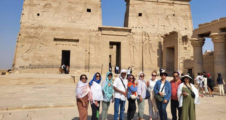 Un groupe de touristes se tient devant les pylônes en grès et les bas-reliefs du temple de Philae par une journée ensoleillée.