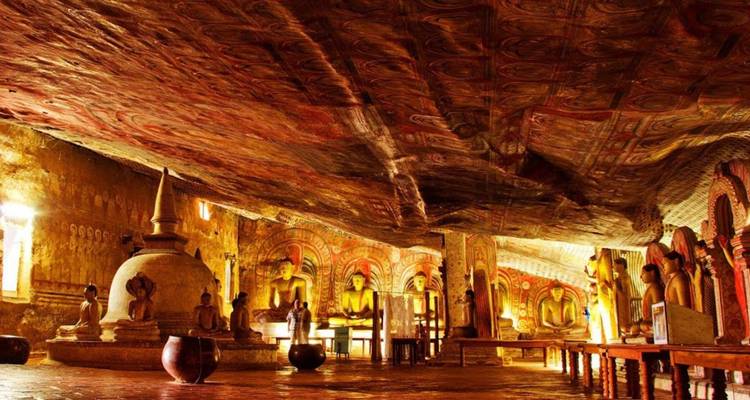 Verlichte binnenkant van de grottempel van Dambulla met gouden beelden en kleurrijke plafondmuurschilderingen.