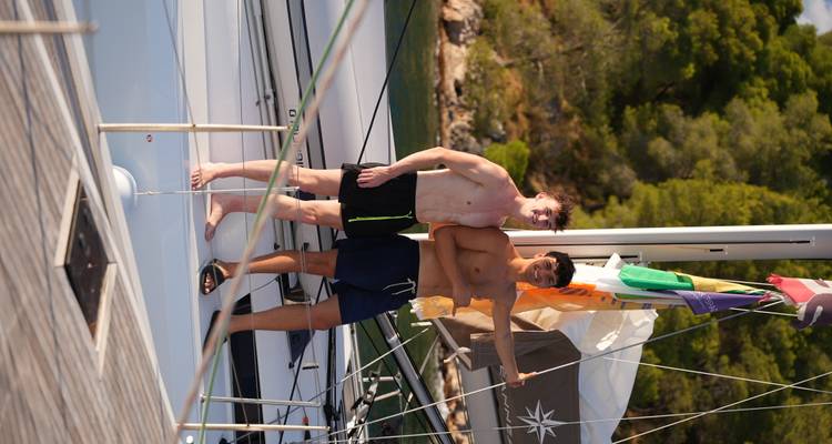 Repeat shot of two friends posing shirtless on a sailboat deck in summer light.