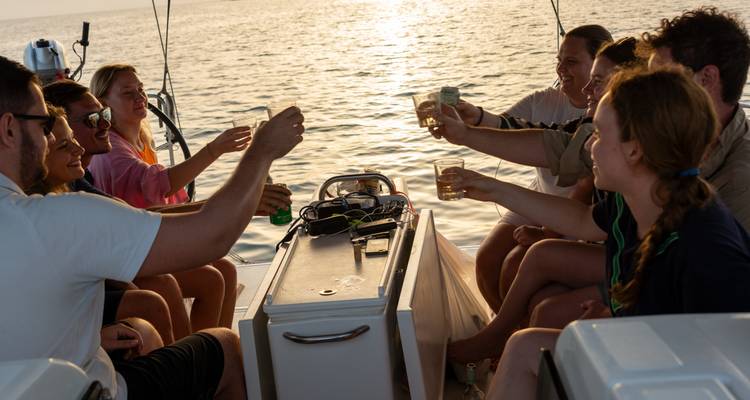 Group of sailors raising drinks together in a cockpit at sunset over calm sea.