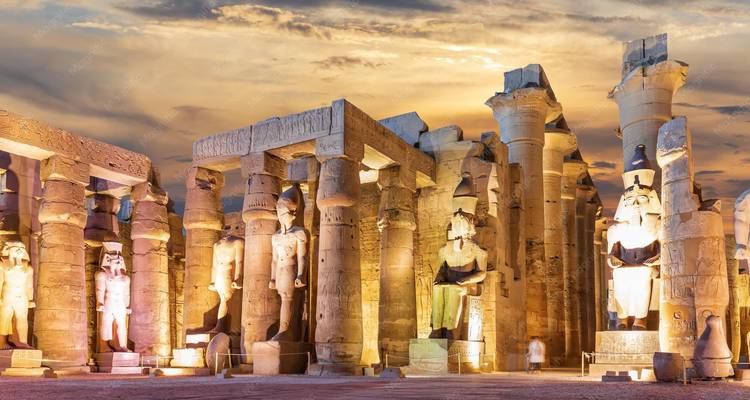 Beleuchtete Säulen und Statuen des Luxor-Tempels in der Dämmerung unter glühendem Himmel.