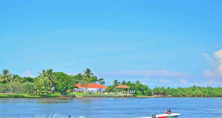 Una lancha rápida remolcando a un esquiador acuático en una laguna tranquila con playas bordeadas de palmeras y villas.