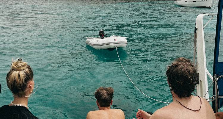 Travellers on a yacht watch a small dinghy floating on clear blue water