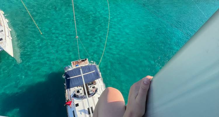 High viewpoint looking down a yacht mast to turquoise water while a hand grips the rigging