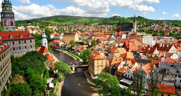 Panoramic view of Cesky Krumlov’s red-tiled roofs, winding river and castle tower under bright skies.
