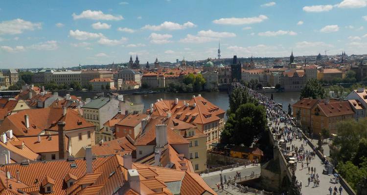 Daytime panoramic of Prague’s terracotta rooftops and crowded Charles Bridge crossing the Vltava.