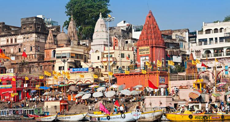 Busy ghats of Varanasi with colorful temples, flags and crowd by the river.