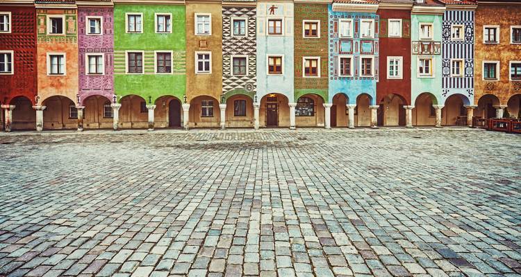 Des maisons de ville historiques colorées dotées d'arcades bordent une place pavée de galets déserte.