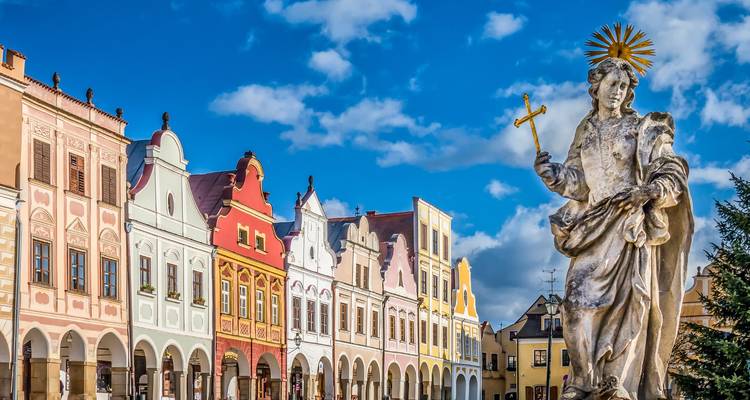 Rangée de maisons Renaissance aux couleurs pastel sur la place de Telc avec une statue ornée d'un saint au premier plan.