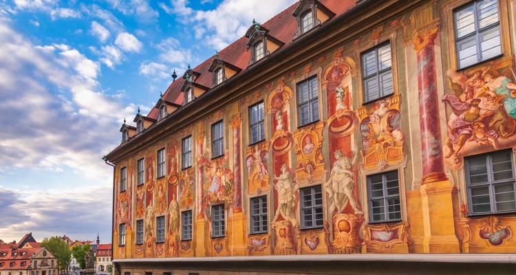 Fachada elaboradamente decorada con frescos del Ayuntamiento Antiguo de Bamberg bajo un cielo parcialmente nublado.