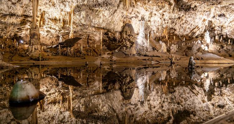 Grotte de calcaire illuminée avec des stalactites parfaitement reflétées dans un lac souterrain.