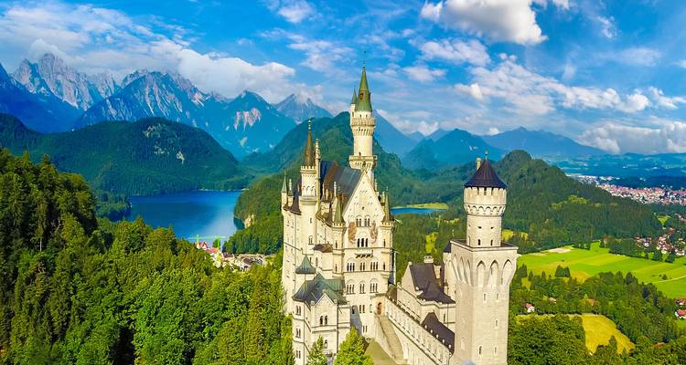 Luchtfoto van kasteel Neuschwanstein met uitzicht op een blauw alpenmeer en een ruw berglandschap.