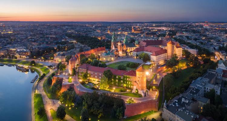 Vista aérea al atardecer del complejo del Castillo de Wawel brillando sobre Cracovia con la curva del río visible.