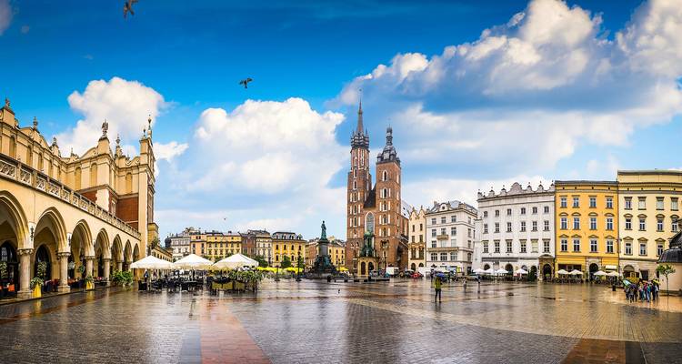 Toma panorámica amplia de la Plaza Principal de Mercado de Cracovia después de la lluvia, reflejando torres góticas y la lonja de paños.