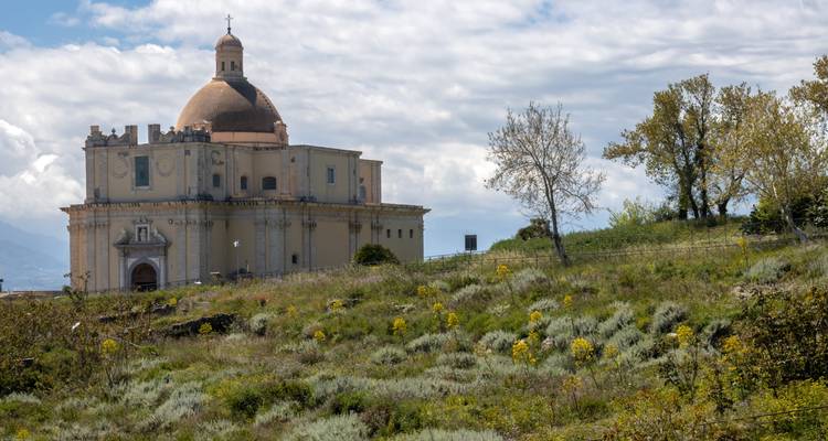 Geïsoleerde heuveltopkerk met koepeldak dat uitkijkt over wilde bloemenweides en verre wolken.