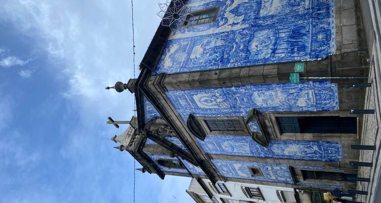 Vista completa de la iglesia de azulejos Capela das Almas bajo el cielo azul con la cruz silueteada.