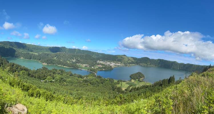 Vista panorámica de los lagos gemelos azul y verde del cráter de Sete Cidades rodeados de colinas verdes bajo un cielo despejado.