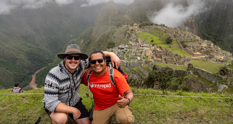 Deux randonneurs posent joyeusement sur une crête avec une vue panoramique brumeuse de Machu Picchu bien en dessous.
