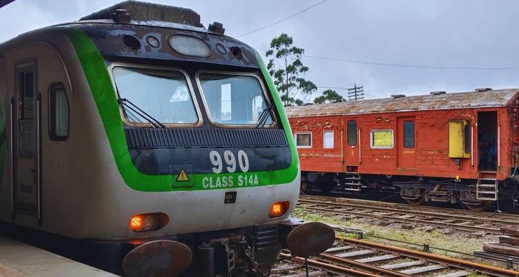 Moderne groen-en-zilveren passagierstrein geparkeerd naast oudere rode wagons op een landelijk station