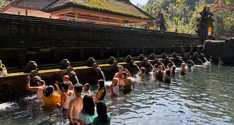 Des fidèles se tenant jusqu'à la taille dans un bassin de pierre dans un temple balinais, recevant de l'eau provenant de gargouilles sculptées