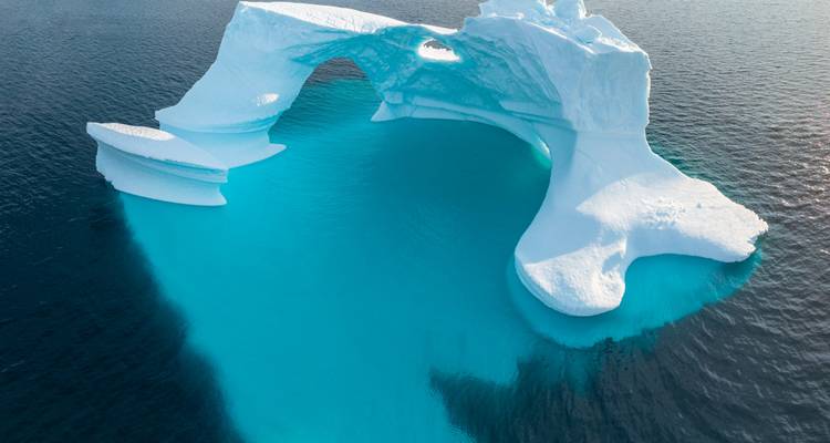 Ein auffälliger türkis- und weißer Eisbergbogen schwebt in dunklen arktischen Gewässern.