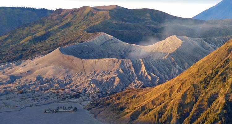 Dramatic view of smoking volcanic caldera and ridges glowing in warm light.
