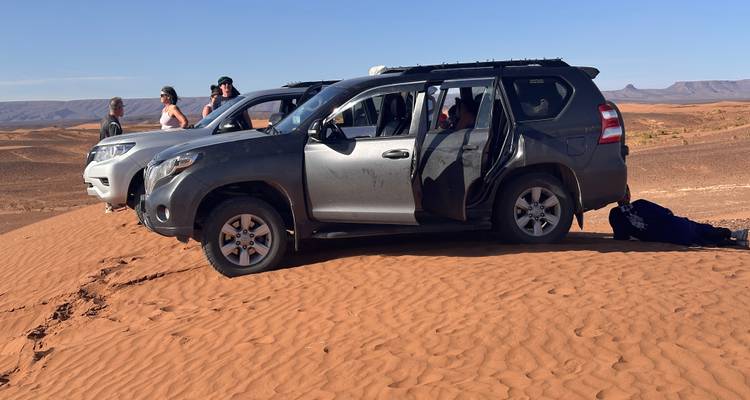 4x4 vehicles and passengers parked atop a dune during a desert off-road excursion.
