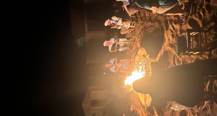Travellers and local musicians sitting around a glowing campfire in the desert at night.