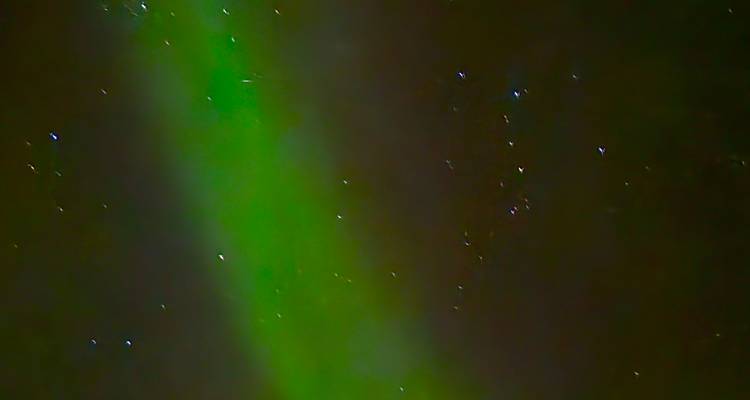 Légère traînée d'aurore boréale verte floue et étoiles faibles dans le ciel nocturne.