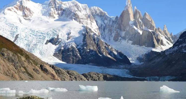 Des icebergs flottent sur un lac gris tranquille sous des pics enneigés dentelés à la lumière cristalline de Patagonie.