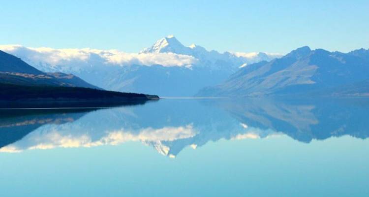 Le lac aux eaux parfaitement lisses reflète fidèlement le Mont Cook enneigé et les pics environnants sous un ciel bleu.