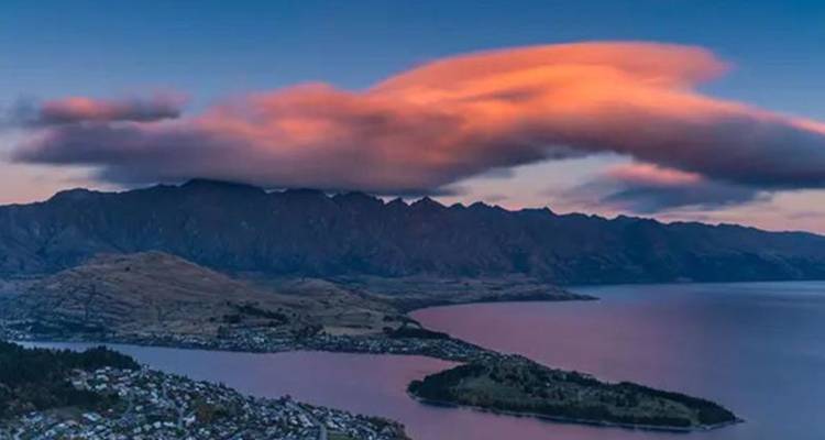 Les nuages du crépuscule teintés de rose flottent au-dessus de Queenstown et du lac Wakatipu avec une chaîne de montagnes en silhouette.
