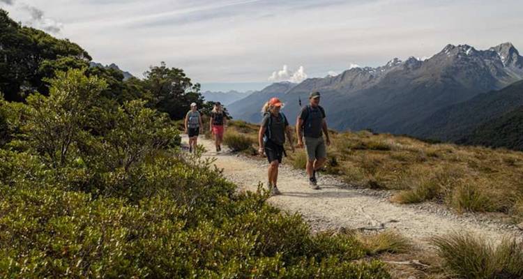 Randonnées en petit groupe le long d'un sentier alpin avec des pics dentelés lointains sous de fins nuages.