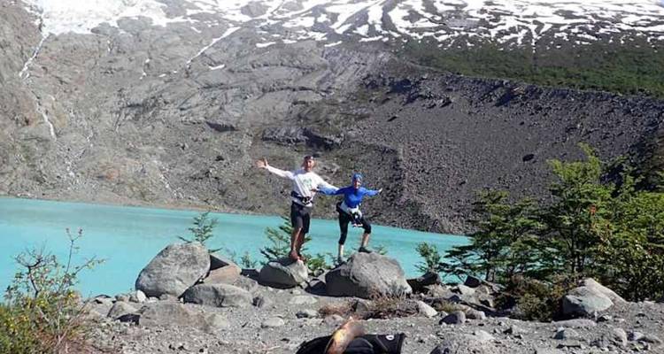 Deux randonneurs posent sur des rochers au bord d'un lac alpin d'un bleu turquoise éclatant avec des montagnes rocheuses aux sommets enneigés derrière eux.