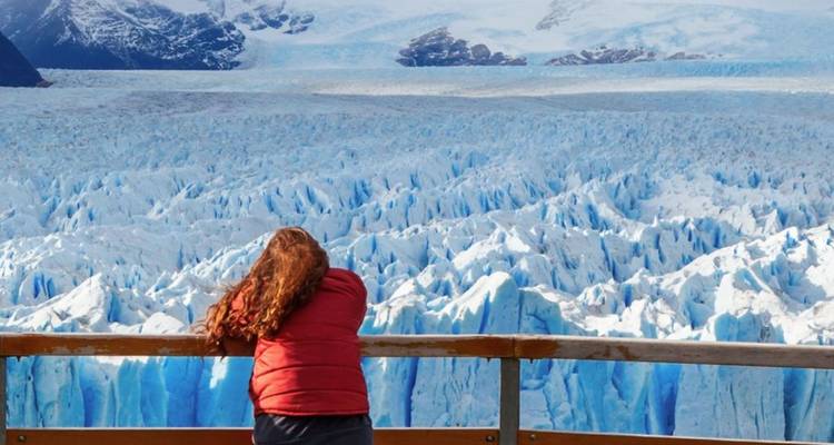 Un voyageur s'appuie sur une rambarde en bois qui surplombe les immenses crevasses bleues du glacier Perito Moreno.