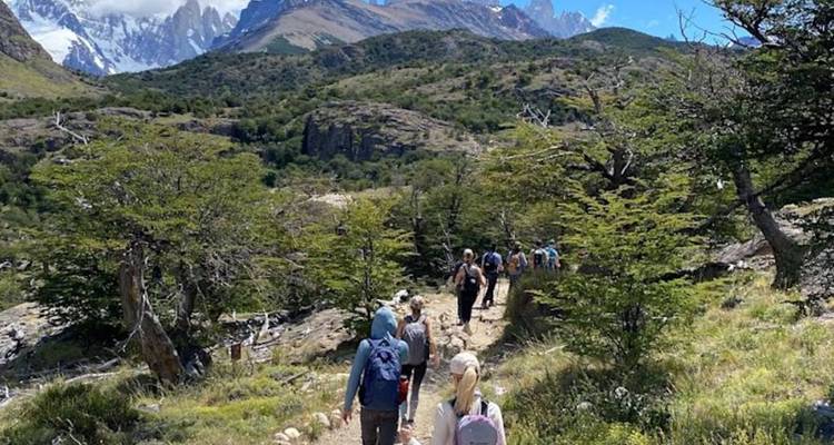 Une file de randonneurs monte sur un sentier forestier avec des pics de granit dentelés qui s'élèvent dramatiquement à l'horizon.